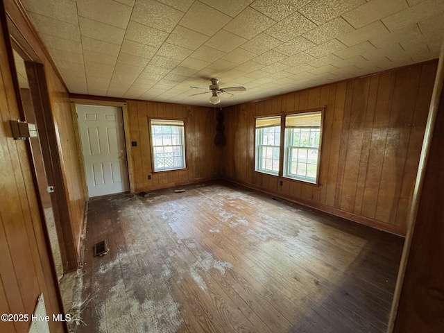 unfurnished room featuring hardwood / wood-style flooring, ceiling fan, and wood walls