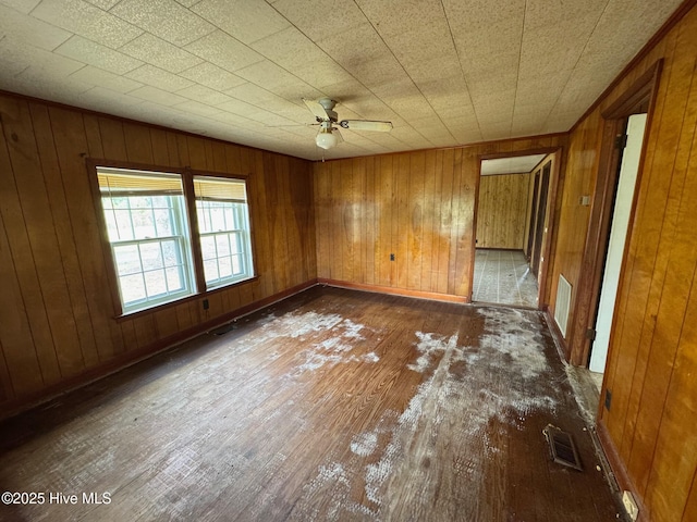 empty room featuring hardwood / wood-style flooring, ceiling fan, wood walls, and baseboards