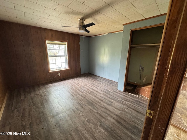 unfurnished bedroom featuring wood finished floors, ornamental molding, a closet, wooden walls, and ceiling fan