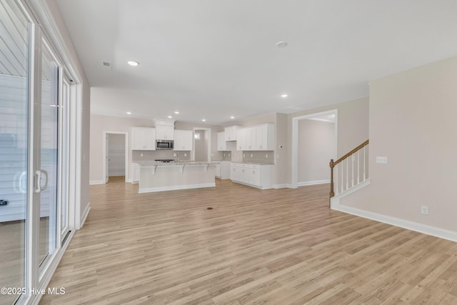 unfurnished living room with light wood-style flooring, baseboards, stairs, and recessed lighting