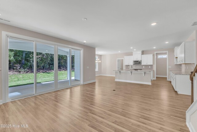 unfurnished living room featuring light wood-style flooring, recessed lighting, baseboards, a chandelier, and a sink