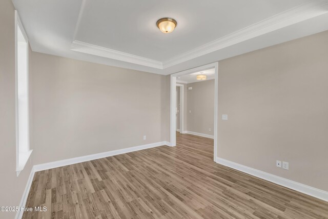 unfurnished room featuring wood finished floors, ornamental molding, baseboards, and a raised ceiling
