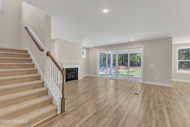unfurnished living room with light wood-type flooring, baseboards, stairs, and recessed lighting