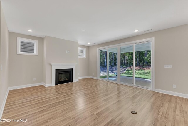 unfurnished living room featuring light wood-style flooring, baseboards, a glass covered fireplace, and recessed lighting