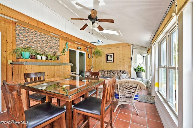 dining room with wooden walls, healthy amount of natural light, ceiling fan, lofted ceiling, and tile patterned floors