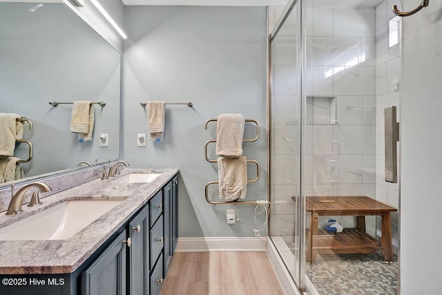 bathroom featuring a stall shower, baseboards, double vanity, and wood finished floors