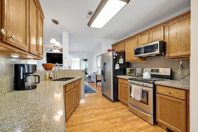 kitchen with appliances with stainless steel finishes, a sink, brown cabinets, tasteful backsplash, and hanging light fixtures