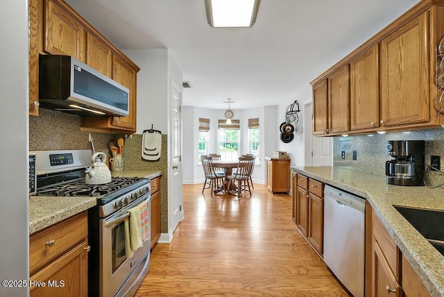 kitchen featuring stainless steel appliances, light wood-type flooring, brown cabinets, and backsplash
