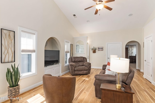 living area featuring a ceiling fan, arched walkways, plenty of natural light, light wood-type flooring, and high vaulted ceiling