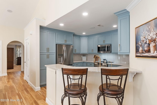 kitchen with stainless steel appliances, blue cabinets, a peninsula, arched walkways, and light stone countertops