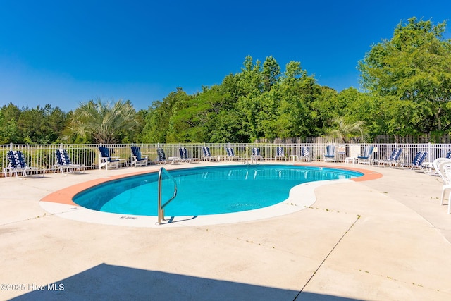 community pool featuring fence, a patio area, and view of wooded area