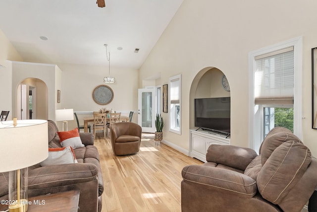 living area featuring light wood finished floors, arched walkways, high vaulted ceiling, and baseboards