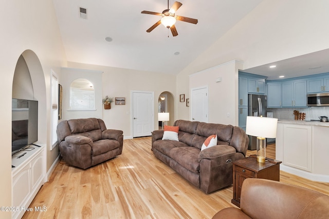 living area featuring arched walkways, a ceiling fan, high vaulted ceiling, light wood-style floors, and baseboards