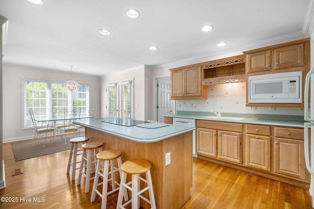 kitchen with white microwave, a sink, a center island, light wood finished floors, and ornamental molding