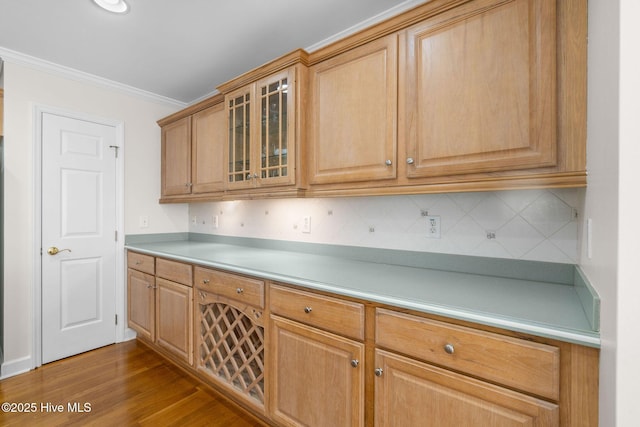 kitchen with glass insert cabinets, wood finished floors, ornamental molding, light countertops, and decorative backsplash