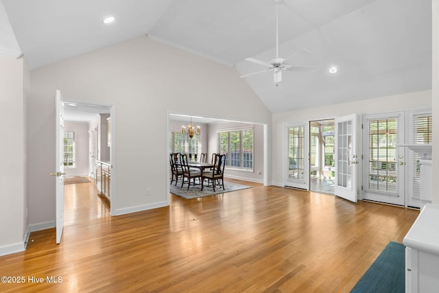 living room with healthy amount of natural light, high vaulted ceiling, ceiling fan, a chandelier, and light wood-style floors