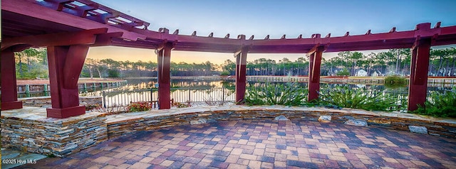 patio terrace at dusk with a pergola, a water view, and fence