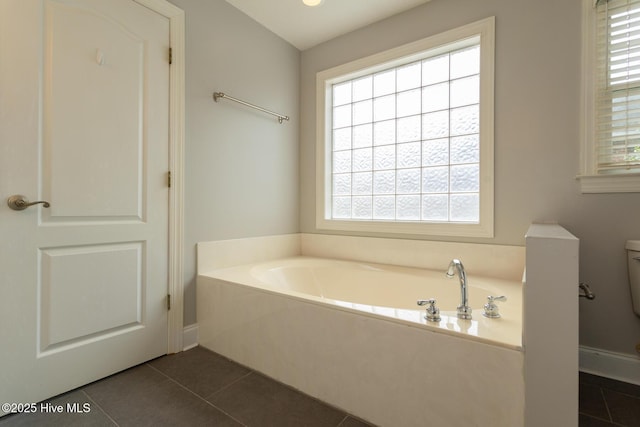 bathroom with tile patterned flooring, a bath, toilet, and baseboards