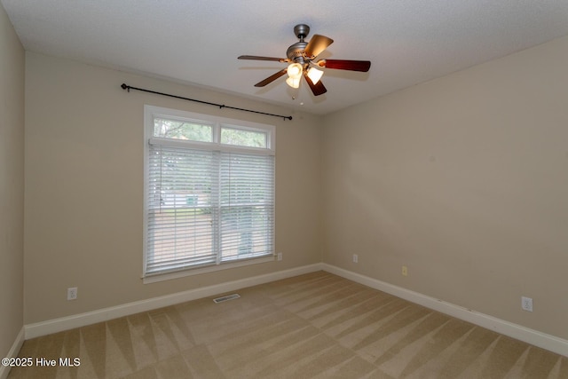 spare room with light colored carpet, a ceiling fan, and baseboards
