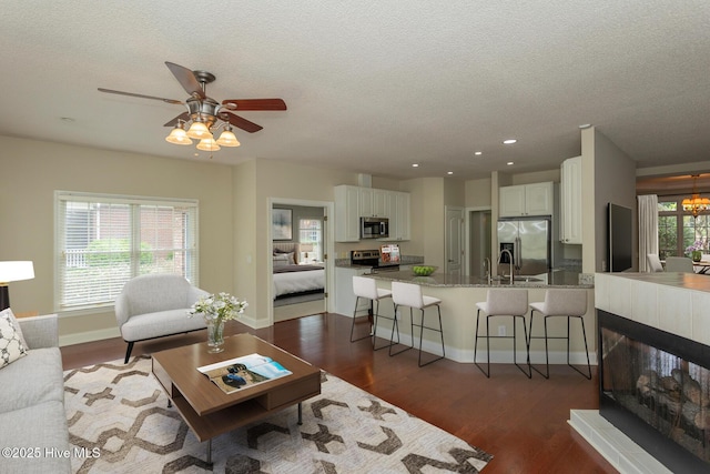 living area with dark wood-style flooring, a textured ceiling, baseboards, a ceiling fan, and recessed lighting
