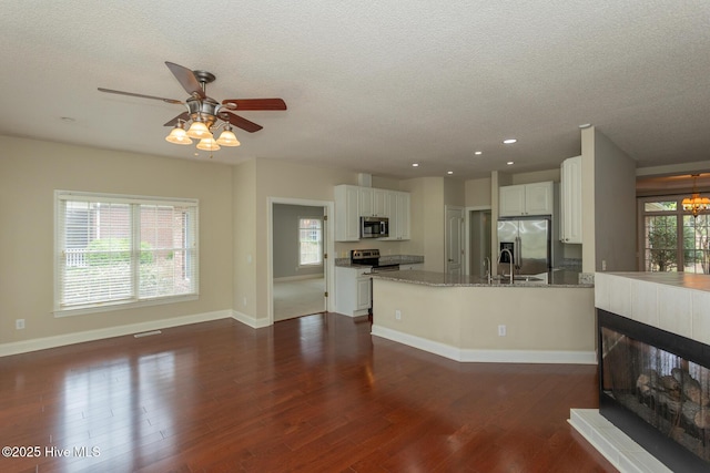kitchen with appliances with stainless steel finishes, a textured ceiling, dark wood-style flooring, white cabinets, and a sink