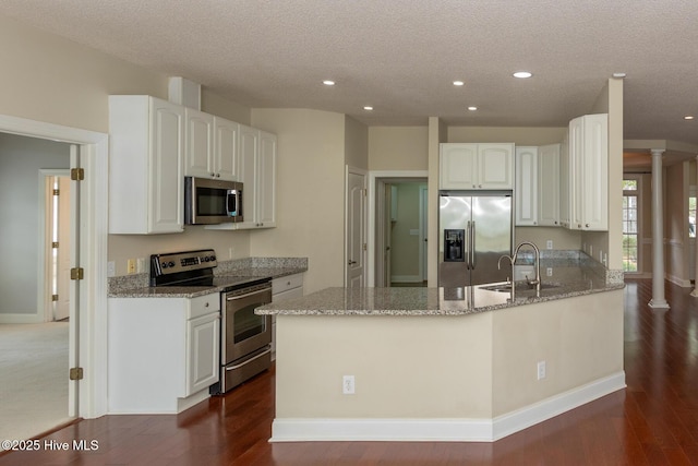 kitchen with appliances with stainless steel finishes, light stone counters, a sink, a peninsula, and a textured ceiling