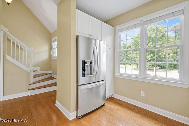 kitchen featuring stainless steel refrigerator with ice dispenser, baseboards, light wood-type flooring, white cabinetry, and vaulted ceiling