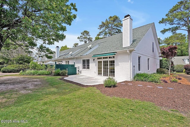 rear view of house with brick siding, a patio area, a chimney, and a shingled roof
