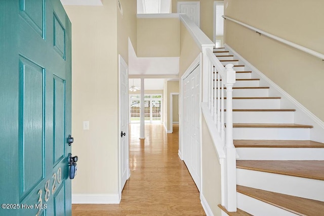 entryway with stairs, light wood finished floors, a towering ceiling, and baseboards