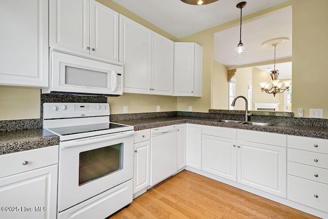 kitchen featuring white appliances, a sink, a chandelier, dark countertops, and white cabinets