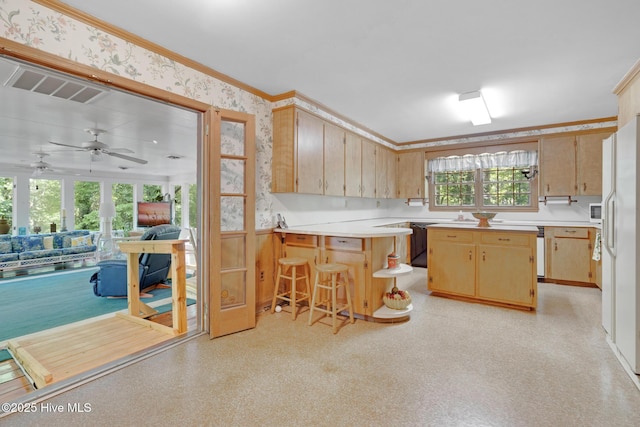 kitchen with wallpapered walls, a peninsula, light countertops, light brown cabinets, and crown molding