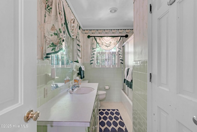 full bath with toilet, tile walls, vanity, tile patterned flooring, and enclosed tub / shower combo