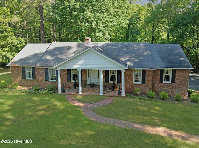 view of front of home with a front yard, brick siding, a porch, a chimney, and roof with shingles