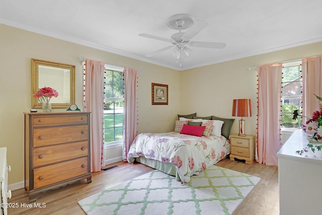 bedroom with light wood-style floors, ornamental molding, multiple windows, and ceiling fan