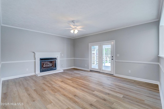 unfurnished living room with a ceiling fan, light wood finished floors, a fireplace with raised hearth, baseboards, and ornamental molding
