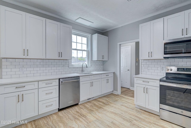 kitchen with appliances with stainless steel finishes, a sink, light countertops, decorative backsplash, and crown molding