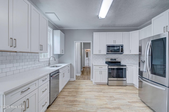 kitchen featuring stainless steel appliances, a sink, white cabinetry, light countertops, and a textured ceiling