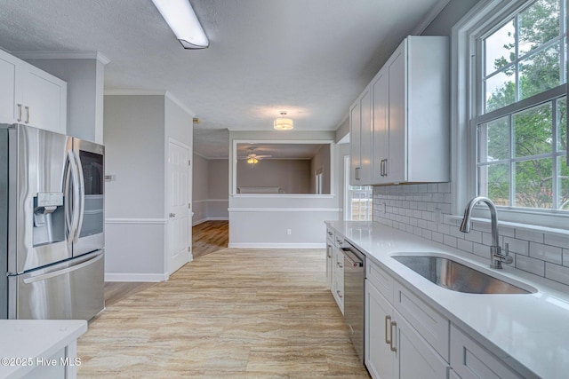 kitchen featuring stainless steel appliances, a sink, light countertops, a ceiling fan, and tasteful backsplash