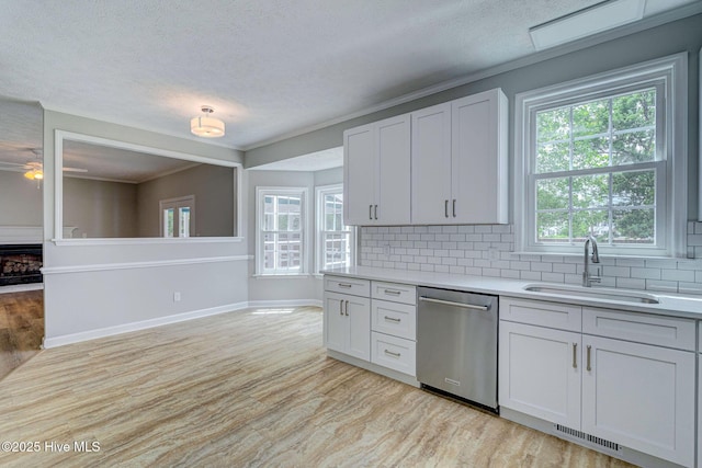 kitchen featuring stainless steel dishwasher, a sink, light countertops, light wood-style flooring, and a textured ceiling