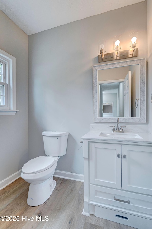 half bath featuring wood finished floors, baseboards, and toilet