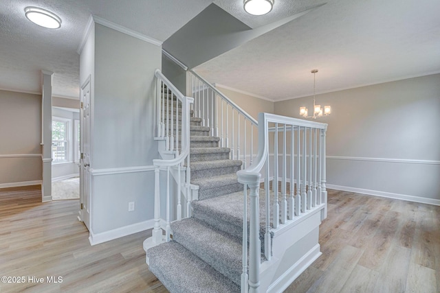 stairs featuring wood finished floors, baseboards, a chandelier, a textured ceiling, and crown molding