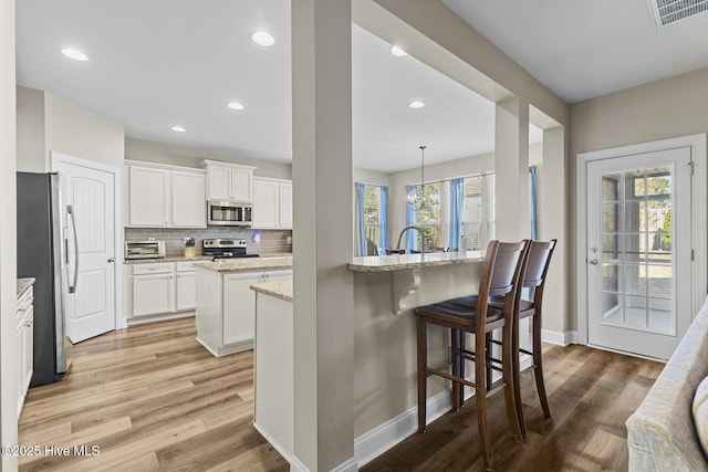 211 Willow Ridge Dr, Holly Ridge, NC 28445 - kitchen with stainless steel appliances, a kitchen island with sink, baseboards, light wood-style floors, and light stone counters