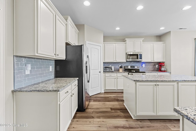 211 Willow Ridge Dr, Holly Ridge, NC 28445 - kitchen featuring stainless steel appliances, white cabinets, tasteful backsplash, light wood-style floors, and a kitchen island