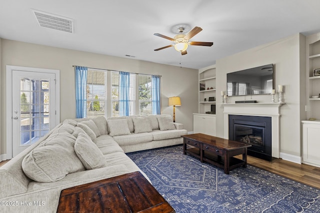 211 Willow Ridge Dr, Holly Ridge, NC 28445 - living area with ceiling fan, dark wood-type flooring, built in features, a glass covered fireplace, and baseboards