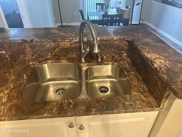 kitchen view of a sink, dark stone counters, white cabinetry, and baseboards