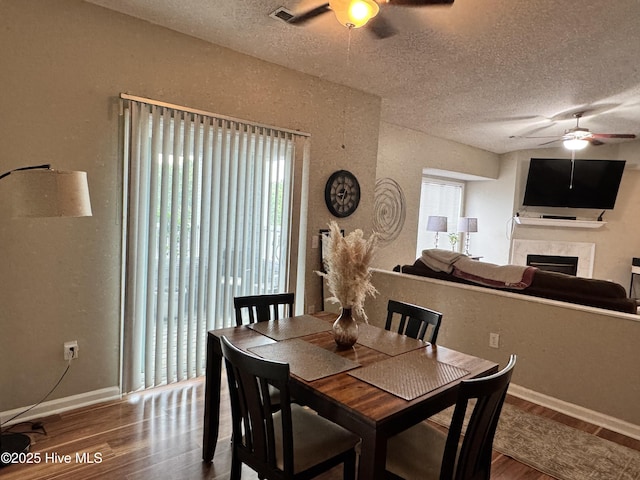 dining space featuring a ceiling fan, wood finished floors, a textured ceiling, and a tiled fireplace