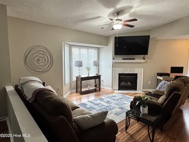 living room with wood finished floors, a ceiling fan, a premium fireplace, a textured ceiling, and baseboards