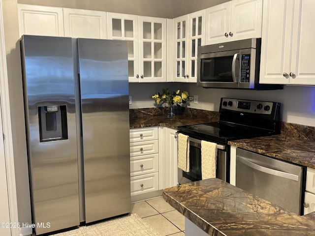 kitchen featuring stainless steel appliances, white cabinets, glass insert cabinets, light tile patterned flooring, and dark stone counters