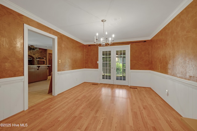 unfurnished dining area featuring wainscoting, a chandelier, wood finished floors, french doors, and ornamental molding