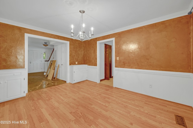 unfurnished dining area featuring light wood-type flooring, a chandelier, wainscoting, ornamental molding, and stairs